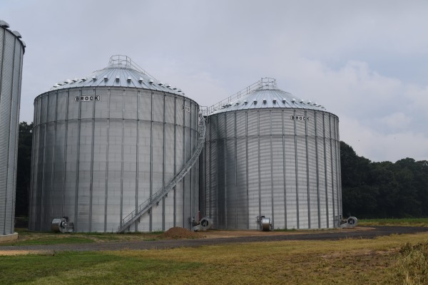 two Brock grain bins next to each other in front of the woods