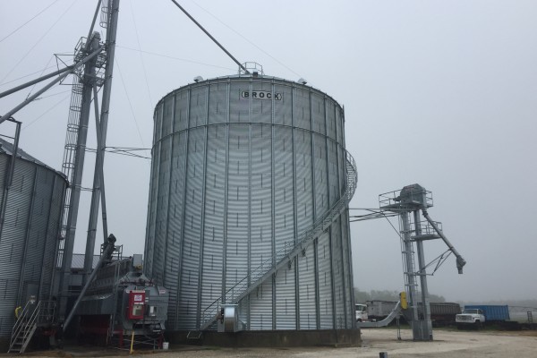 Brock grain bin in front of a cloudy sky with work trucks parked by it