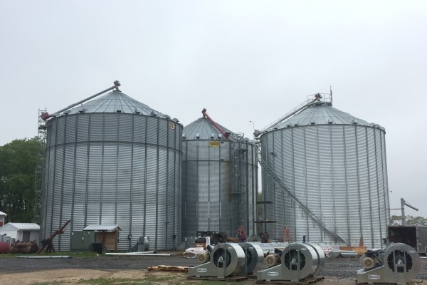 three Brock grain bins with dryers in front of them