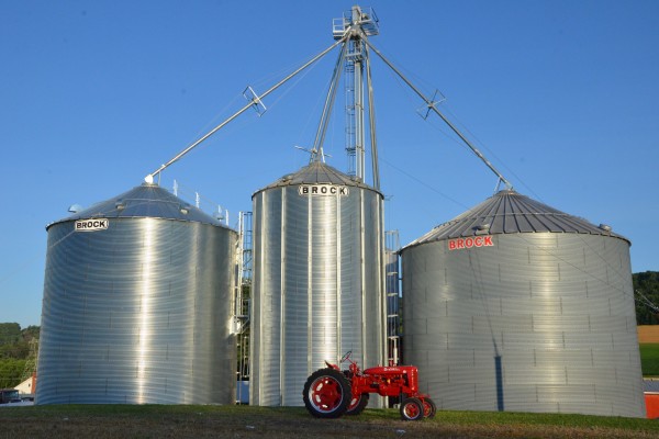 red tractor in front of three Brock grain bins